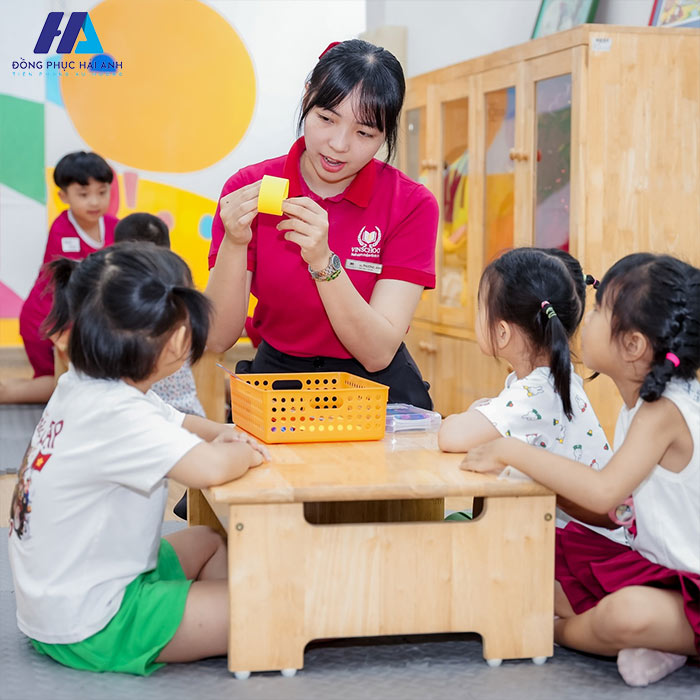 Đồng phục giáo viên mầm non Vinschool gồm áo thun polo có cổ màu đỏ tươi, trên áo có in logo của trường